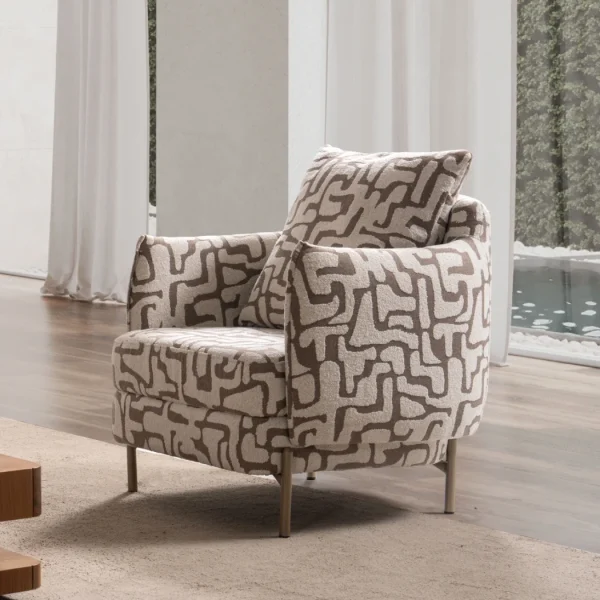 A modern accent armchair featuring an abstract geometric pattern upholstery, rounded continuous armrests, a matching throw cushion, and slim metallic tapered legs set in a brightly lit interior.