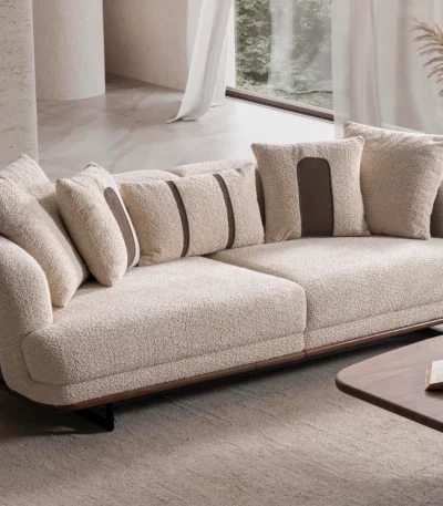 Sola Two Seater Sofa featuring rounded armrests, plush back cushions, and a wooden base trim in a modern living room setting.