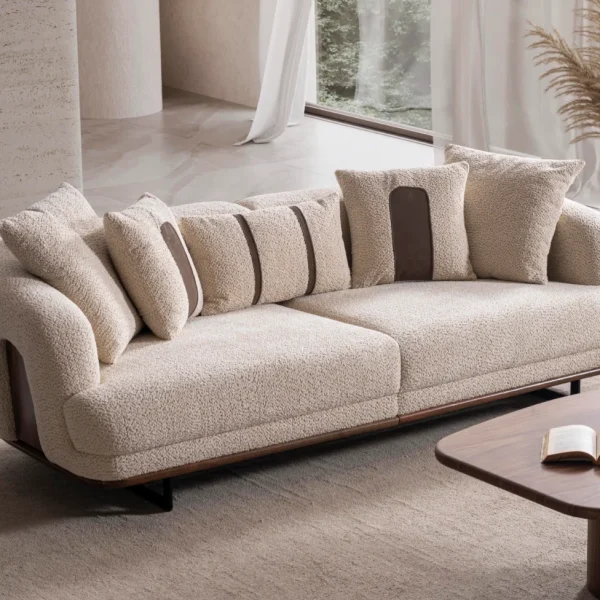 Sola Two Seater Sofa featuring rounded armrests, plush back cushions, and a wooden base trim in a modern living room setting.