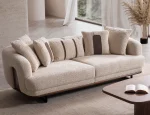Sola Two Seater Sofa featuring rounded armrests, plush back cushions, and a wooden base trim in a modern living room setting.