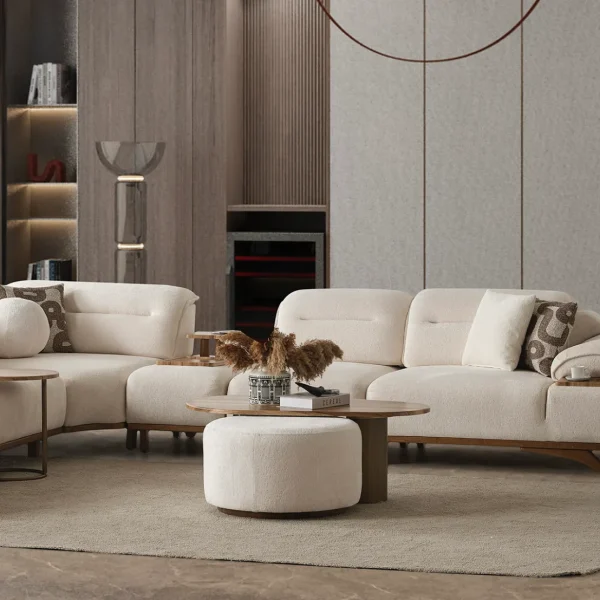 A modern living room featuring the Grace Sofa. The arrangement displays a plush taupe sofa and a matching cream sofa, both designed with distinctive integrated wooden side tables on the armrests and angled wooden legs. A white swivel armchair and a round wooden coffee table complete the cozy, contemporary look of this furniture from Turkey.