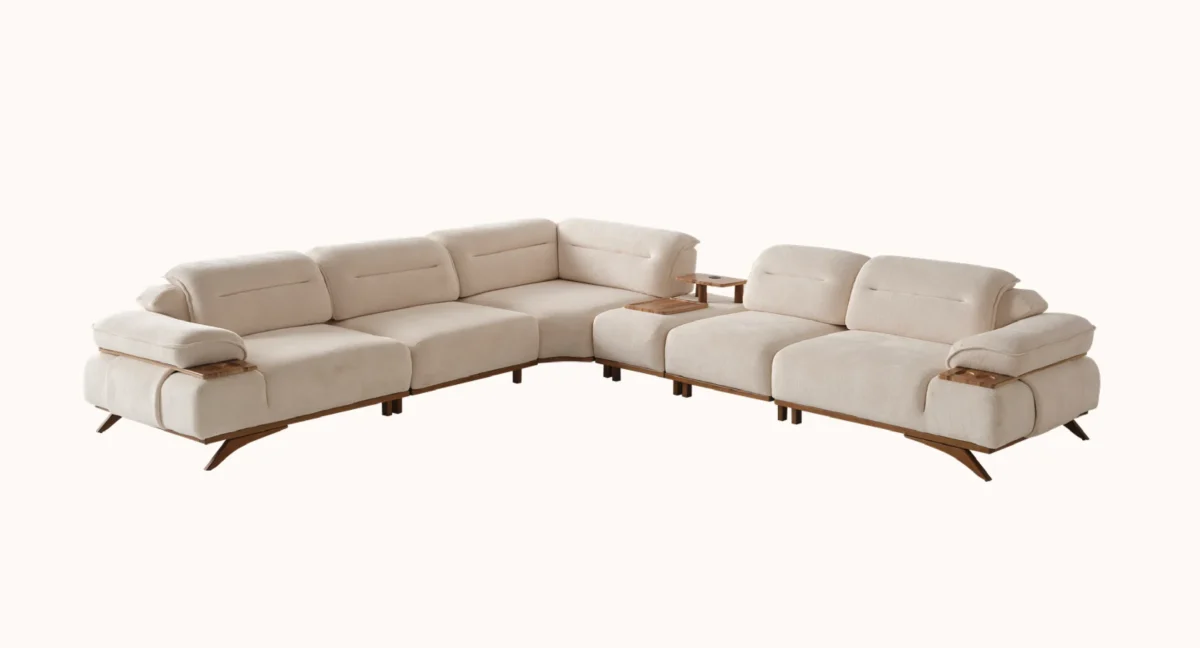 A modern living room featuring the Grace Sofa. The arrangement displays a plush taupe sofa and a matching cream sofa, both designed with distinctive integrated wooden side tables on the armrests and angled wooden legs. A white swivel armchair and a round wooden coffee table complete the cozy, contemporary look of this furniture from Turkey.