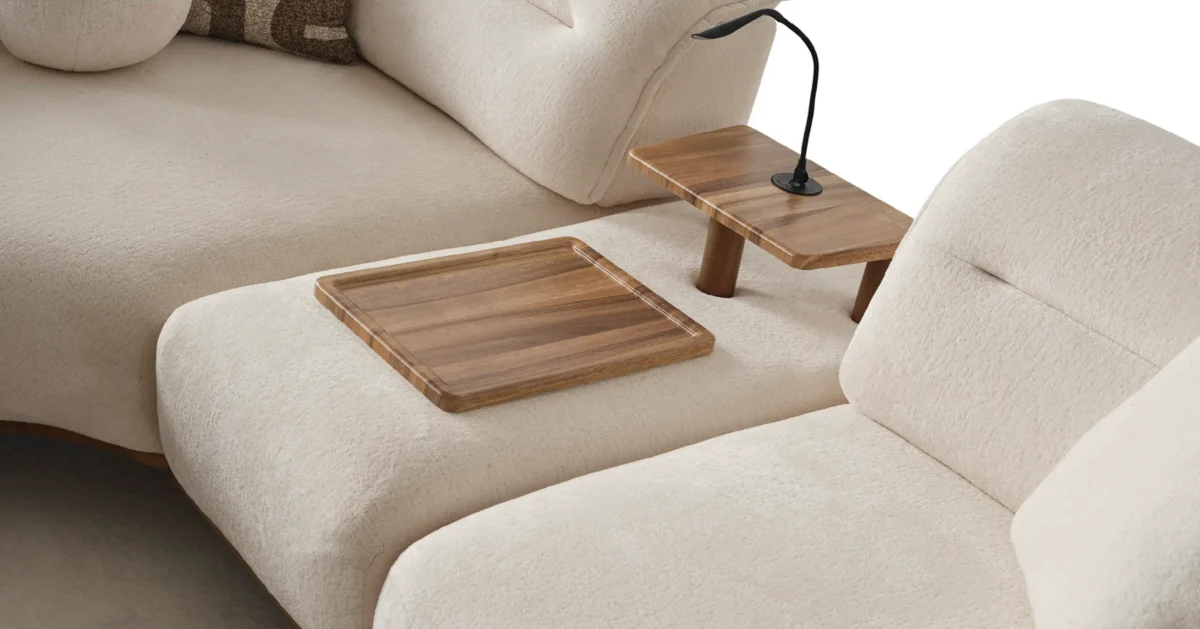A modern living room featuring the Grace Sofa. The arrangement displays a plush taupe sofa and a matching cream sofa, both designed with distinctive integrated wooden side tables on the armrests and angled wooden legs. A white swivel armchair and a round wooden coffee table complete the cozy, contemporary look of this furniture from Turkey.