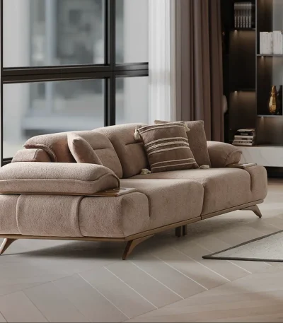 A modern living room featuring the Grace Sofa. The arrangement displays a plush taupe sofa and a matching cream sofa, both designed with distinctive integrated wooden side tables on the armrests and angled wooden legs. A white swivel armchair and a round wooden coffee table complete the cozy, contemporary look of this furniture from Turkey.
