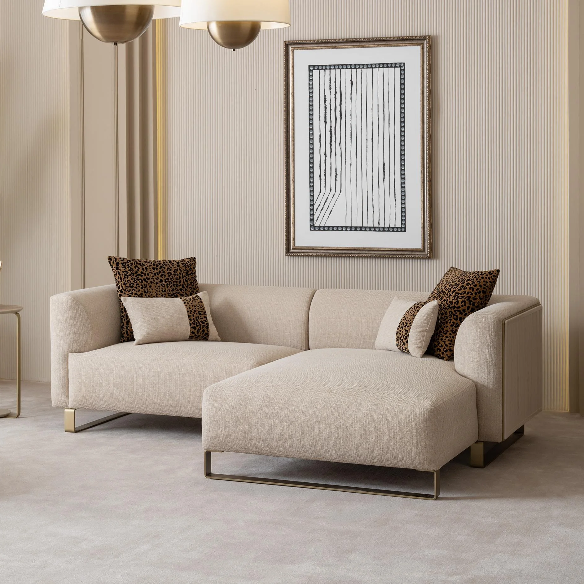 Grandeur-Corner-Sofa-Living-Room-Furniture-Turkey-1 A luxurious modular Grandeur sofa set in a bright, modern living room. The set features cream-colored fabric upholstery with rectangular cushions and sleek gold metallic legs. Beside the modular sections sits a matching rounded armchair with gold accents. The scene includes minimalist decor, a marble coffee table, and large windows, highlighting the elegant design of the Grandeur furniture from Turkey.