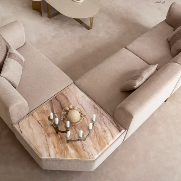 A luxurious modular Grandeur sofa set in a bright, modern living room. The set features cream-colored fabric upholstery with rectangular cushions and sleek gold metallic legs. Beside the modular sections sits a matching rounded armchair with gold accents. The scene includes minimalist decor, a marble coffee table, and large windows, highlighting the elegant design of the Grandeur furniture from Turkey.