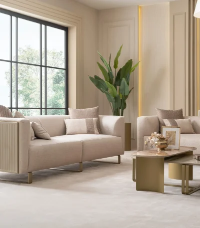 A luxurious modular Grandeur sofa set in a bright, modern living room. The set features cream-colored fabric upholstery with rectangular cushions and sleek gold metallic legs. Beside the modular sections sits a matching rounded armchair with gold accents. The scene includes minimalist decor, a marble coffee table, and large windows, highlighting the elegant design of the Grandeur furniture from Turkey.