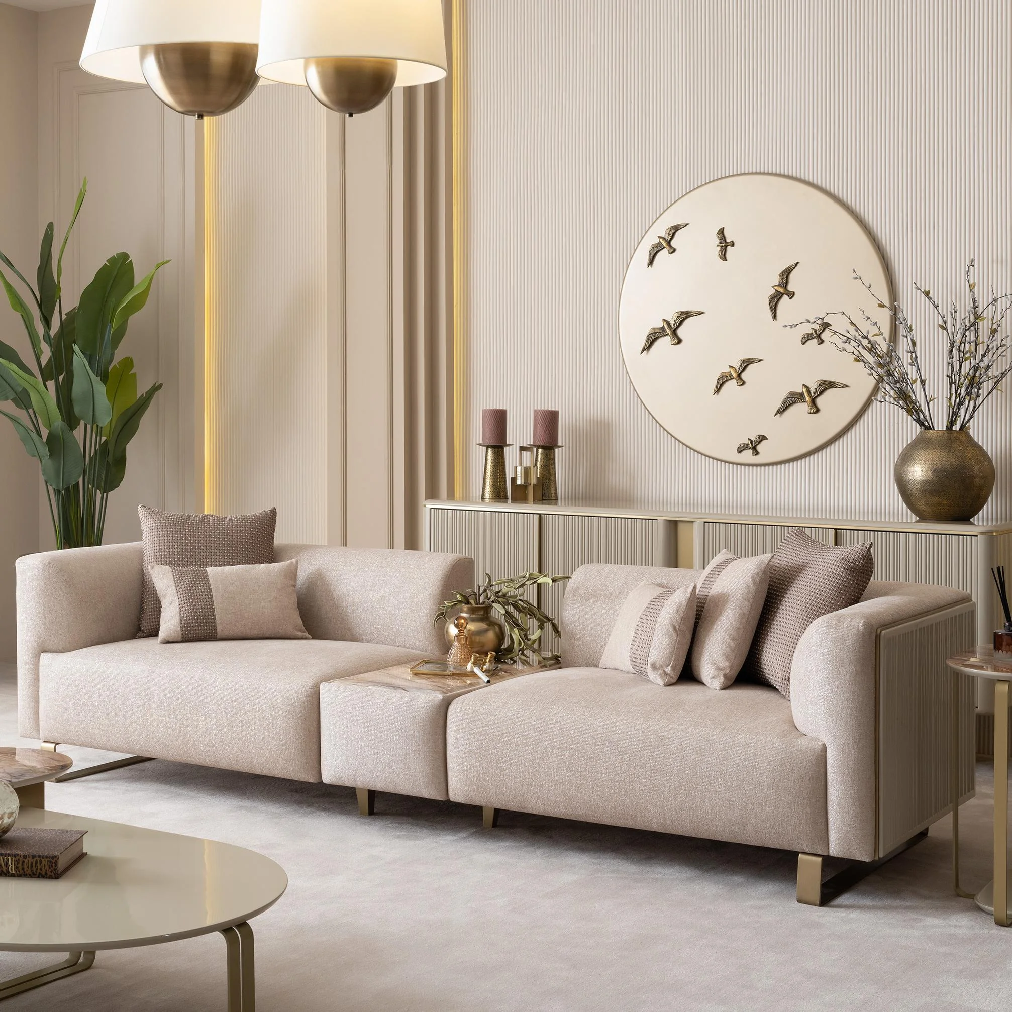 Grandeur-Sofa-With-Module-Living-Room-Furniture-Turkey-1 A luxurious modular Grandeur sofa set in a bright, modern living room. The set features cream-colored fabric upholstery with rectangular cushions and sleek gold metallic legs. Beside the modular sections sits a matching rounded armchair with gold accents. The scene includes minimalist decor, a marble coffee table, and large windows, highlighting the elegant design of the Grandeur furniture from Turkey.