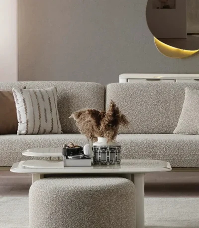 A modern Horizon Sofa set arranged in a chic living room. The furniture features textured grey upholstery with distinctive folded armrests and sleek champagne gold metallic legs. A matching round swivel armchair and a white coffee table with a cylindrical pouf complete the contemporary Turkish furniture ensemble.