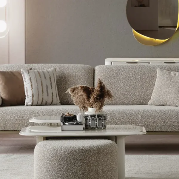 A modern Horizon Sofa set arranged in a chic living room. The furniture features textured grey upholstery with distinctive folded armrests and sleek champagne gold metallic legs. A matching round swivel armchair and a white coffee table with a cylindrical pouf complete the contemporary Turkish furniture ensemble.