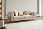 Luxia Sofa Set featuring a charcoal velvet three-seater, a blush pink loveseat with geometric patterns, and matching armchairs. The set is detailed with gold-toned metal bases and frames, set in a neoclassical room with arched windows and ornate wall moldings.