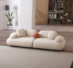 Alba Sofa Set featuring a large cream bouclé sectional, a matching loveseat, and a geometric patterned accent chair. The set is arranged in a spacious, modern room with high ceilings, an arched alcove, and a large library bookshelf.