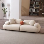 Alba Sofa Set featuring a large cream bouclé sectional, a matching loveseat, and a geometric patterned accent chair. The set is arranged in a spacious, modern room with high ceilings, an arched alcove, and a large library bookshelf.