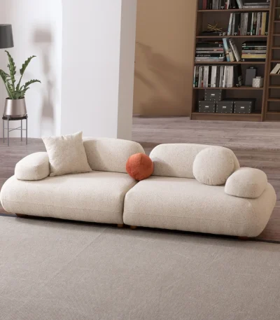 Alba Sofa Set featuring a large cream bouclé sectional, a matching loveseat, and a geometric patterned accent chair. The set is arranged in a spacious, modern room with high ceilings, an arched alcove, and a large library bookshelf.