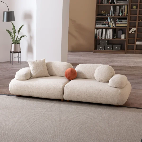 Alba Sofa Set featuring a large cream bouclé sectional, a matching loveseat, and a geometric patterned accent chair. The set is arranged in a spacious, modern room with high ceilings, an arched alcove, and a large library bookshelf.