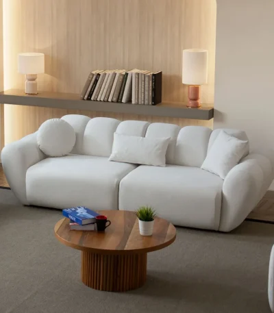 Alure Sofa Set featuring a crisp white three-seater sofa, a soft sage green loveseat, and a matching white armchair. The pieces showcase deep vertical stitching and a plush, rounded design, centered around a fluted wooden coffee table in a minimalist, warm-toned living room.