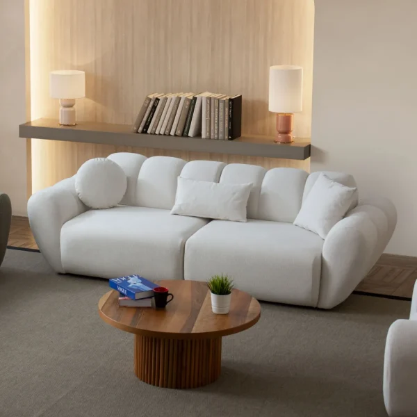 Alure Sofa Set featuring a crisp white three-seater sofa, a soft sage green loveseat, and a matching white armchair. The pieces showcase deep vertical stitching and a plush, rounded design, centered around a fluted wooden coffee table in a minimalist, warm-toned living room.