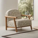 The organic Areon Armchair featuring textured fabric and wooden legs, placed in a bright, minimalist living room that evokes a sense of natural harmony and peace.