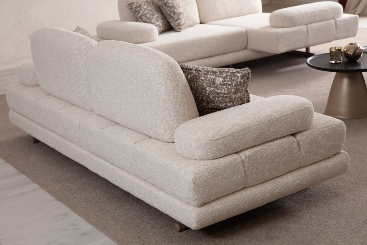 A modern textured fabric sofa featuring linear tufted backrest detailing, soft rounded side armrests supported by slim elegant wooden-accent legs, set in a spacious high-ceiling living room environment.