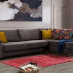 Bria Corner Sofa modern charcoal grey sectional sofa featuring quilted outer armrests, colorful throw pillows, and wooden legs.