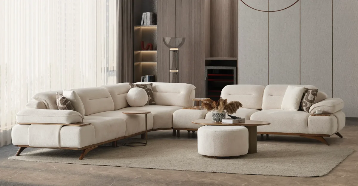 A modern living room featuring the Grace Sofa. The arrangement displays a plush taupe sofa and a matching cream sofa, both designed with distinctive integrated wooden side tables on the armrests and angled wooden legs. A white swivel armchair and a round wooden coffee table complete the cozy, contemporary look of this furniture from Turkey.