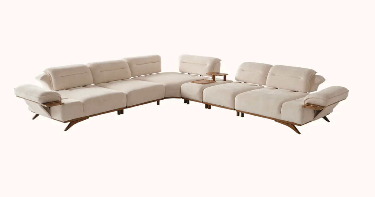 A modern living room featuring the Grace Sofa. The arrangement displays a plush taupe sofa and a matching cream sofa, both designed with distinctive integrated wooden side tables on the armrests and angled wooden legs. A white swivel armchair and a round wooden coffee table complete the cozy, contemporary look of this furniture from Turkey.