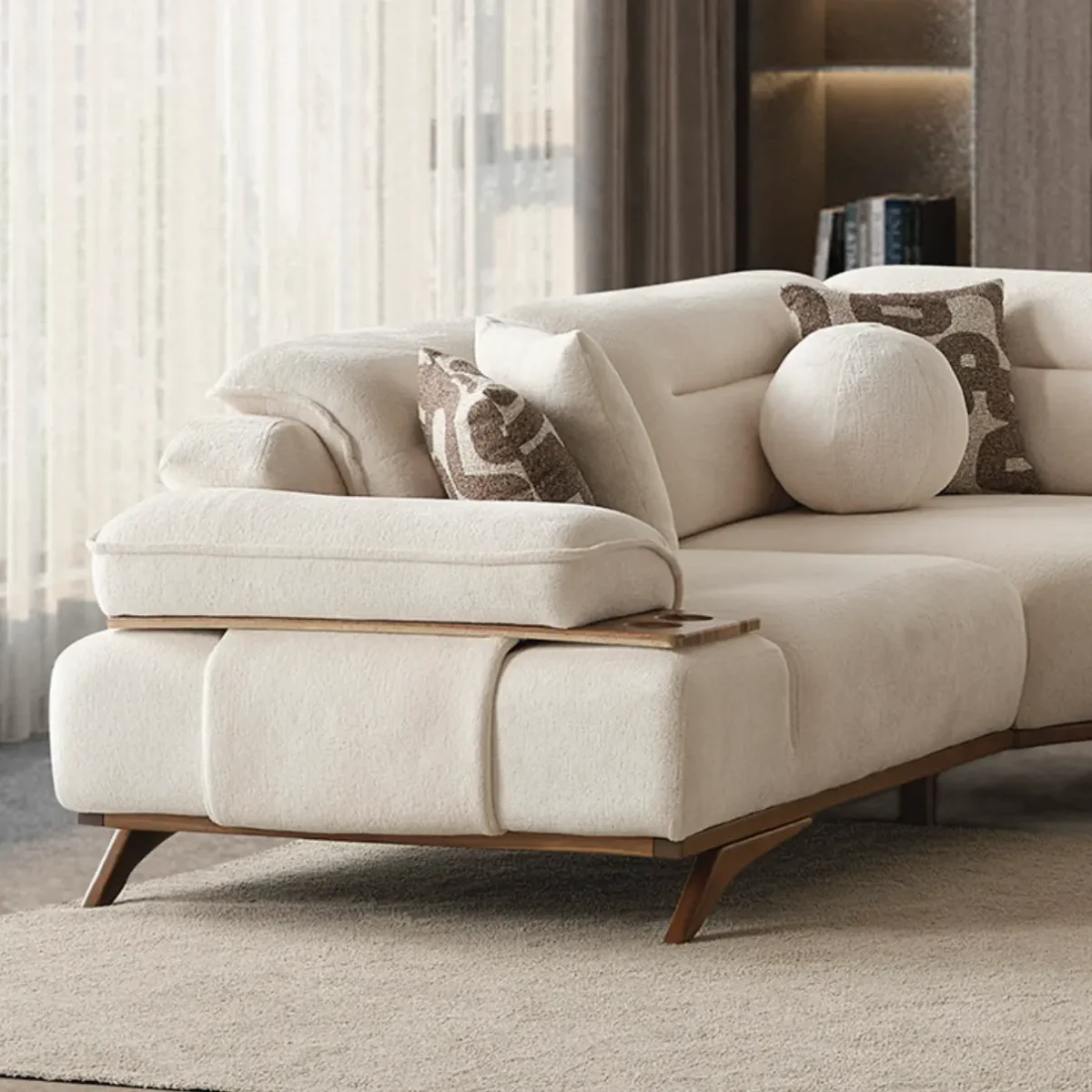 A modern living room featuring the Grace Sofa. The arrangement displays a plush taupe sofa and a matching cream sofa, both designed with distinctive integrated wooden side tables on the armrests and angled wooden legs. A white swivel armchair and a round wooden coffee table complete the cozy, contemporary look of this furniture from Turkey.