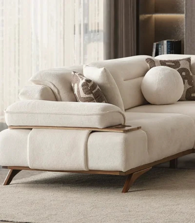 A modern living room featuring the Grace Sofa. The arrangement displays a plush taupe sofa and a matching cream sofa, both designed with distinctive integrated wooden side tables on the armrests and angled wooden legs. A white swivel armchair and a round wooden coffee table complete the cozy, contemporary look of this furniture from Turkey.