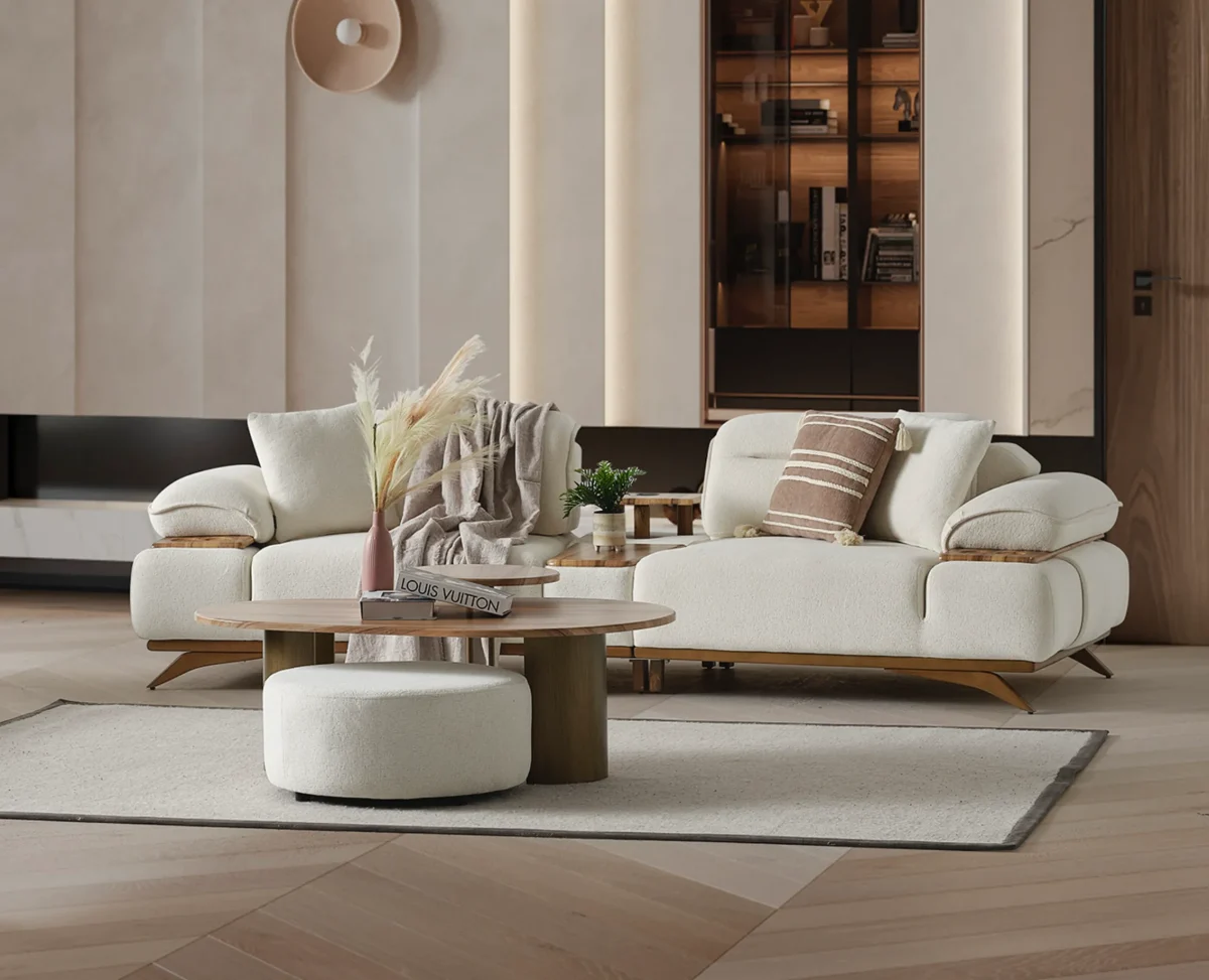 A modern living room featuring the Grace Sofa. The arrangement displays a plush taupe sofa and a matching cream sofa, both designed with distinctive integrated wooden side tables on the armrests and angled wooden legs. A white swivel armchair and a round wooden coffee table complete the cozy, contemporary look of this furniture from Turkey.