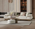 A modern living room featuring the Grace Sofa. The arrangement displays a plush taupe sofa and a matching cream sofa, both designed with distinctive integrated wooden side tables on the armrests and angled wooden legs. A white swivel armchair and a round wooden coffee table complete the cozy, contemporary look of this furniture from Turkey.