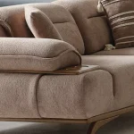 A modern living room featuring the Grace Sofa. The arrangement displays a plush taupe sofa and a matching cream sofa, both designed with distinctive integrated wooden side tables on the armrests and angled wooden legs. A white swivel armchair and a round wooden coffee table complete the cozy, contemporary look of this furniture from Turkey.