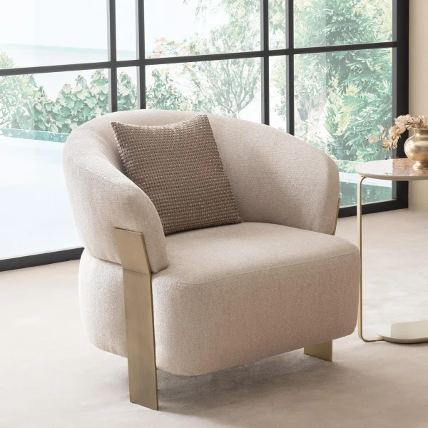 A luxurious modular Grandeur sofa set in a bright, modern living room. The set features cream-colored fabric upholstery with rectangular cushions and sleek gold metallic legs. Beside the modular sections sits a matching rounded armchair with gold accents. The scene includes minimalist decor, a marble coffee table, and large windows, highlighting the elegant design of the Grandeur furniture from Turkey.