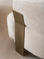 A luxurious modular Grandeur sofa set in a bright, modern living room. The set features cream-colored fabric upholstery with rectangular cushions and sleek gold metallic legs. Beside the modular sections sits a matching rounded armchair with gold accents. The scene includes minimalist decor, a marble coffee table, and large windows, highlighting the elegant design of the Grandeur furniture from Turkey.