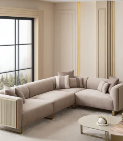 A luxurious modular Grandeur sofa set in a bright, modern living room. The set features cream-colored fabric upholstery with rectangular cushions and sleek gold metallic legs. Beside the modular sections sits a matching rounded armchair with gold accents. The scene includes minimalist decor, a marble coffee table, and large windows, highlighting the elegant design of the Grandeur furniture from Turkey.
