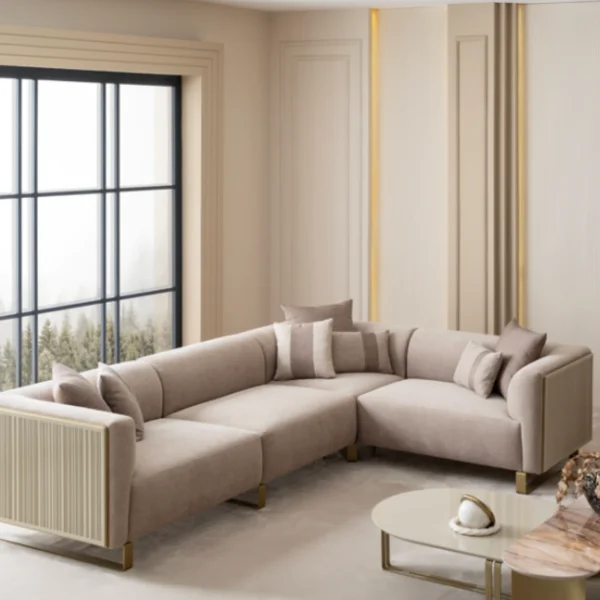 A luxurious modular Grandeur sofa set in a bright, modern living room. The set features cream-colored fabric upholstery with rectangular cushions and sleek gold metallic legs. Beside the modular sections sits a matching rounded armchair with gold accents. The scene includes minimalist decor, a marble coffee table, and large windows, highlighting the elegant design of the Grandeur furniture from Turkey.