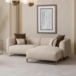 Luksuzna modularna garnitura sofa Grandeur u svetloj, modernoj dnevnoj sobi. Garnitura je presvučena kremastom tkaninom sa pravougaonim jastucima i elegantnim zlatnim metalnim nogama. Pored modularnih delova nalazi se odgovarajuća okrugla fotelja sa zlatnim akcentima. Scena uključuje minimalistički dekor, mermerni stočić za kafu i velike prozore, ističući elegantan dizajn nameštaja Grandeur iz Turske.