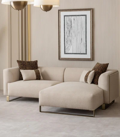 Een luxueuze modulaire Grandeur-bank in een lichte, moderne woonkamer. De set is bekleed met crèmekleurige stof, heeft rechthoekige kussens en slanke gouden metalen poten. Naast de modulaire elementen staat een bijpassende ronde fauteuil met gouden accenten. De minimalistische inrichting, een marmeren salontafel en grote ramen benadrukken het elegante design van de Grandeur-meubelen uit Turkije.