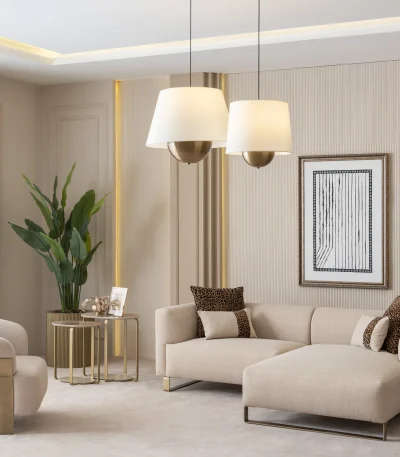 A luxurious modular Grandeur sofa set in a bright, modern living room. The set features cream-colored fabric upholstery with rectangular cushions and sleek gold metallic legs. Beside the modular sections sits a matching rounded armchair with gold accents. The scene includes minimalist decor, a marble coffee table, and large windows, highlighting the elegant design of the Grandeur furniture from Turkey.