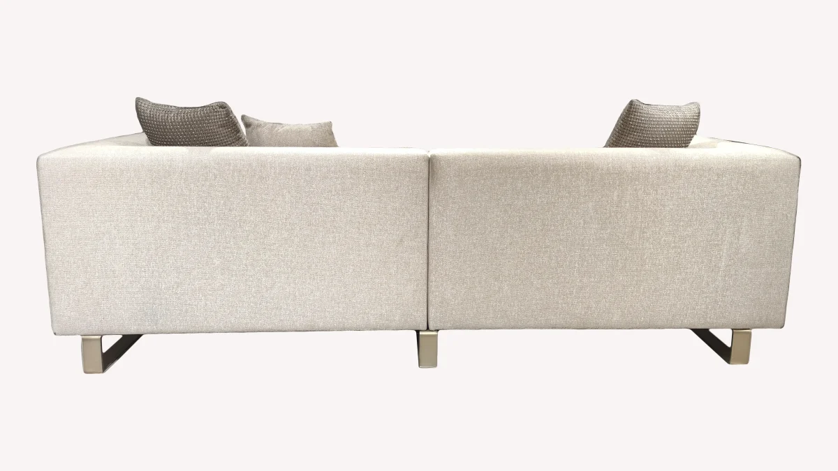 A luxurious modular Grandeur sofa set in a bright, modern living room. The set features cream-colored fabric upholstery with rectangular cushions and sleek gold metallic legs. Beside the modular sections sits a matching rounded armchair with gold accents. The scene includes minimalist decor, a marble coffee table, and large windows, highlighting the elegant design of the Grandeur furniture from Turkey.