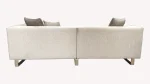 A luxurious modular Grandeur sofa set in a bright, modern living room. The set features cream-colored fabric upholstery with rectangular cushions and sleek gold metallic legs. Beside the modular sections sits a matching rounded armchair with gold accents. The scene includes minimalist decor, a marble coffee table, and large windows, highlighting the elegant design of the Grandeur furniture from Turkey.