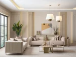A luxurious modular Grandeur sofa set in a bright, modern living room. The set features cream-colored fabric upholstery with rectangular cushions and sleek gold metallic legs. Beside the modular sections sits a matching rounded armchair with gold accents. The scene includes minimalist decor, a marble coffee table, and large windows, highlighting the elegant design of the Grandeur furniture from Turkey.