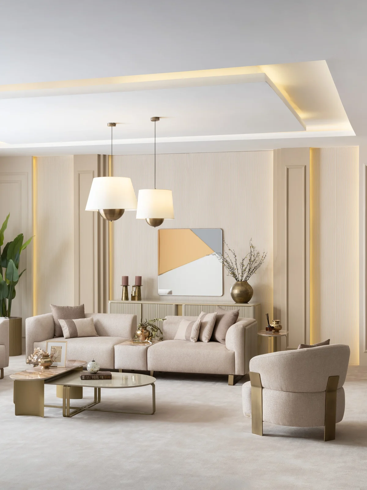 A luxurious modular Grandeur sofa set in a bright, modern living room. The set features cream-colored fabric upholstery with rectangular cushions and sleek gold metallic legs. Beside the modular sections sits a matching rounded armchair with gold accents. The scene includes minimalist decor, a marble coffee table, and large windows, highlighting the elegant design of the Grandeur furniture from Turkey.