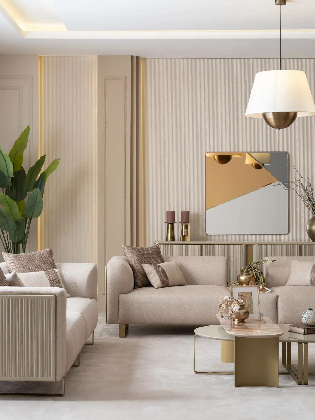 A luxurious modular Grandeur sofa set in a bright, modern living room. The set features cream-colored fabric upholstery with rectangular cushions and sleek gold metallic legs. Beside the modular sections sits a matching rounded armchair with gold accents. The scene includes minimalist decor, a marble coffee table, and large windows, highlighting the elegant design of the Grandeur furniture from Turkey.