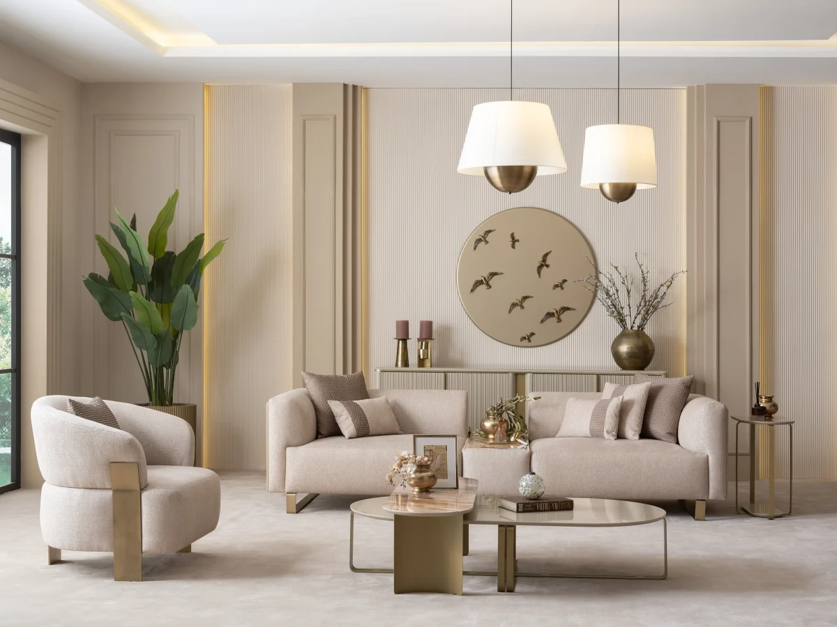 A luxurious modular Grandeur sofa set in a bright, modern living room. The set features cream-colored fabric upholstery with rectangular cushions and sleek gold metallic legs. Beside the modular sections sits a matching rounded armchair with gold accents. The scene includes minimalist decor, a marble coffee table, and large windows, highlighting the elegant design of the Grandeur furniture from Turkey.