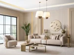 A luxurious modular Grandeur sofa set in a bright, modern living room. The set features cream-colored fabric upholstery with rectangular cushions and sleek gold metallic legs. Beside the modular sections sits a matching rounded armchair with gold accents. The scene includes minimalist decor, a marble coffee table, and large windows, highlighting the elegant design of the Grandeur furniture from Turkey.