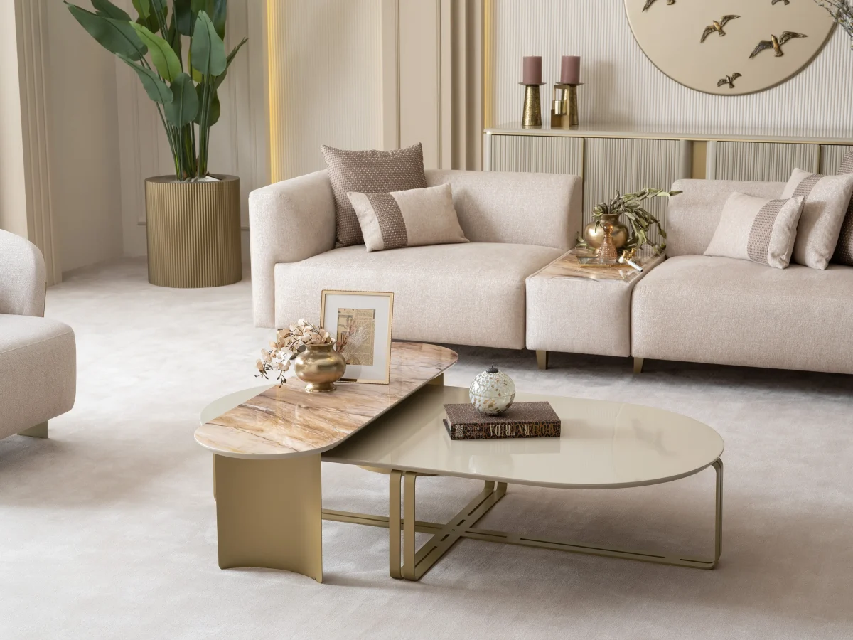 A luxurious modular Grandeur sofa set in a bright, modern living room. The set features cream-colored fabric upholstery with rectangular cushions and sleek gold metallic legs. Beside the modular sections sits a matching rounded armchair with gold accents. The scene includes minimalist decor, a marble coffee table, and large windows, highlighting the elegant design of the Grandeur furniture from Turkey.