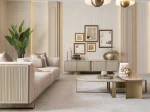 A luxurious modular Grandeur sofa set in a bright, modern living room. The set features cream-colored fabric upholstery with rectangular cushions and sleek gold metallic legs. Beside the modular sections sits a matching rounded armchair with gold accents. The scene includes minimalist decor, a marble coffee table, and large windows, highlighting the elegant design of the Grandeur furniture from Turkey.