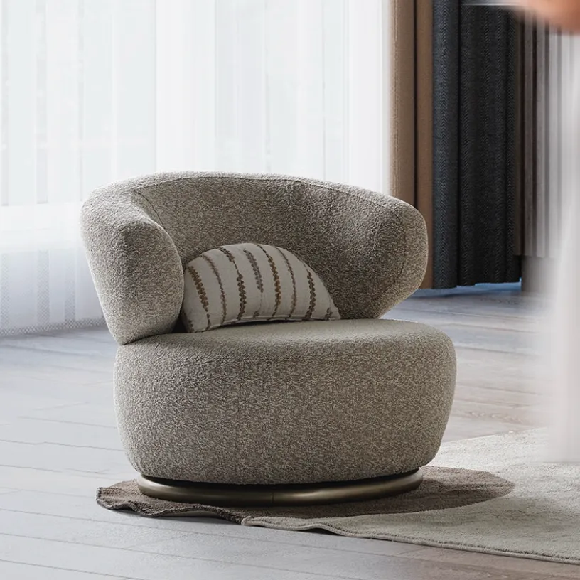 Horizon-Armchair-Modern-Luxury-Sofas-From-Turkey-3 A modern Horizon Sofa set arranged in a chic living room. The furniture features textured grey upholstery with distinctive folded armrests and sleek champagne gold metallic legs. A matching round swivel armchair and a white coffee table with a cylindrical pouf complete the contemporary Turkish furniture ensemble.