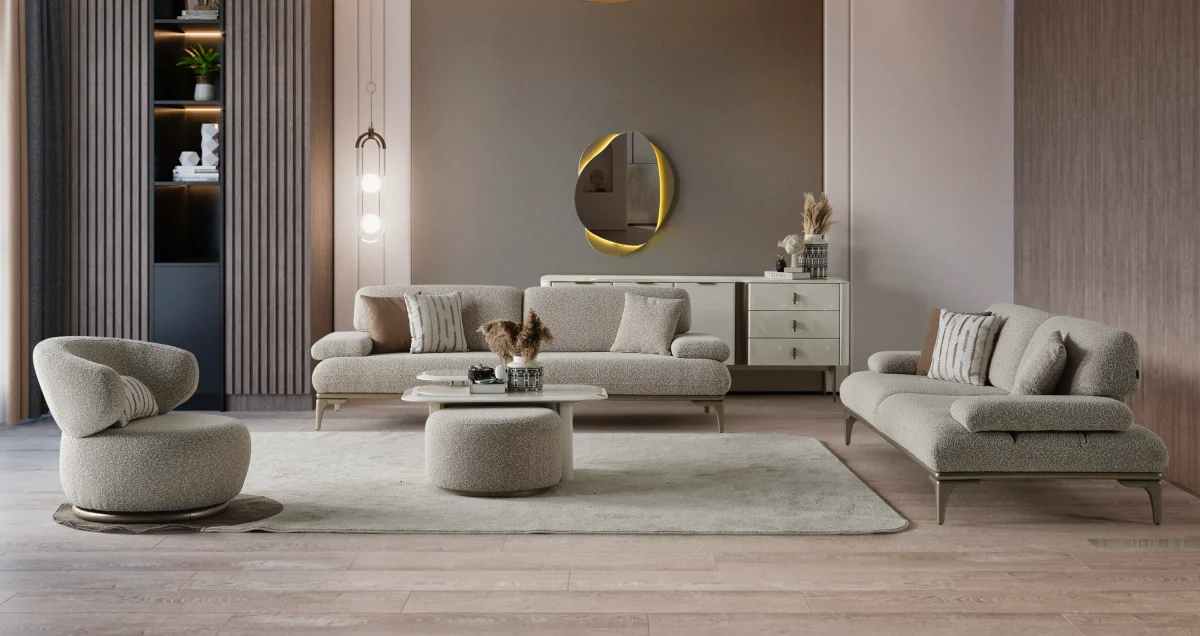 A modern Horizon Sofa set arranged in a chic living room. The furniture features textured grey upholstery with distinctive folded armrests and sleek champagne gold metallic legs. A matching round swivel armchair and a white coffee table with a cylindrical pouf complete the contemporary Turkish furniture ensemble.