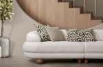 Premium sand grey curved sofa with sculptural round wooden legs and decorative cushions